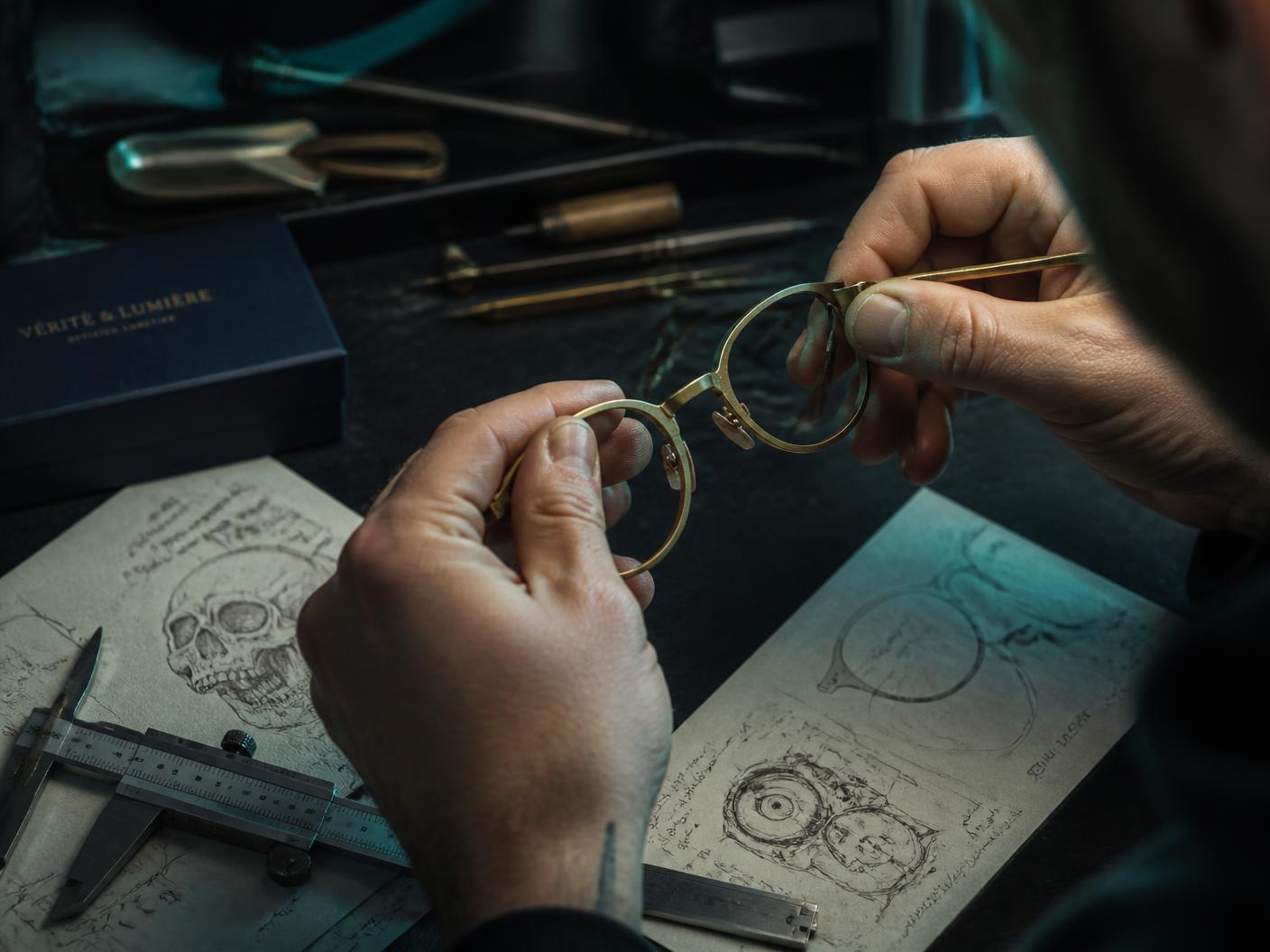 Designer shaping a brass eyewear frame at a workshop bench